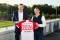 The image shows Andreas Jung, CMO FC Bayern and Thomas Heim, CEO Viessmann Climate Solutions shaking hands in front of a football field while holding a a jersey